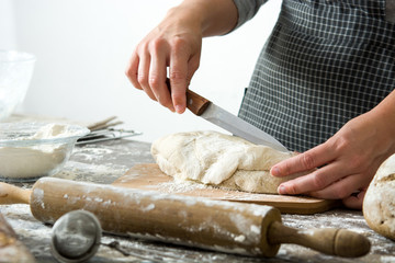 Woman cutting bread dough on wooden table 

