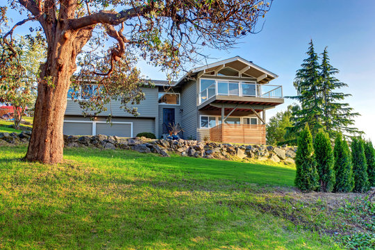 Two Story House Exterior With Gray Siding And Natural Stone Landscape Design.