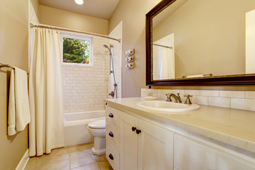 Light bathroom interior with white cabinet and shower with tile wall.