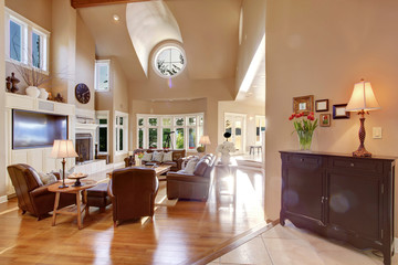 Large living room interior design with high vaulted ceiling and brown leather sofa set.
