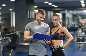 smiling young woman with personal trainer in gym