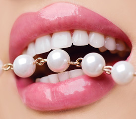 Woman smiles showing white teeth, holding a pearly necklace into the mouth