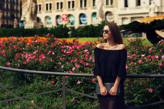 Outdoor summer fashion portrait of young girl posing against bushes of blooming flowers