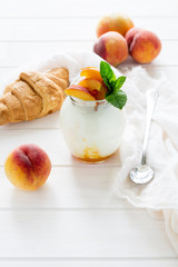 Yogurt with peach in a glass jar on white wooden background. Selective focus