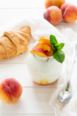 Yogurt with peach in a glass jar on white wooden background. Selective focus