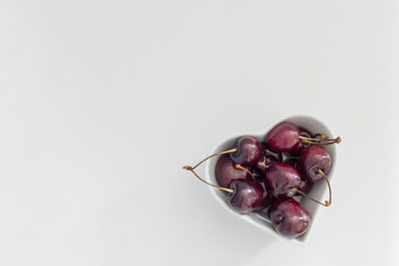 Shining dark cherries in a heart shape bowl on a clear white background