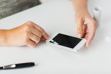 close up of woman with smartphone doing blood test