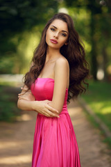 Fototapeta premium Beauty romantic girl outdoor. Pretty young model dressed in long evening dress posing outdoors at path in the park. Full body Portrait with beautiful bokeh