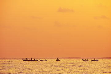 Fototapeta premium silhouettes of fishermen on the boats at sea. Orange sunset lighting. Birds in the sky circling above the boats 