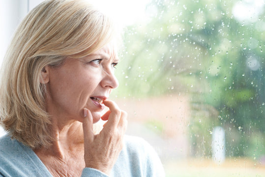 Sad Mature Woman Suffering From Agoraphobia Looking Out Of Windo