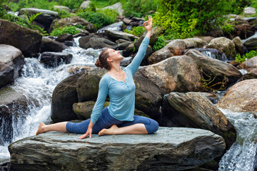 Sorty fit woman doing yoga asana outdoors at tropical waterfall