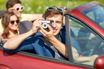 happy friends with camera driving in cabriolet car