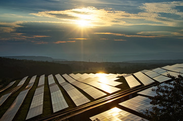Solar power plant between forests at sunset with a star shining rays. The smoking factory chimneys and forested mountains fading into the mist in the distance.