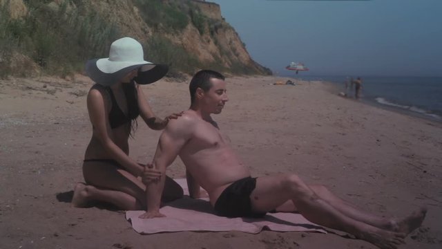 Girl anoints sunscreen on the back of guy while relaxing on the sea beach in summer
