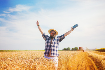 Man on a wheat field holding a tablet, looking excited.