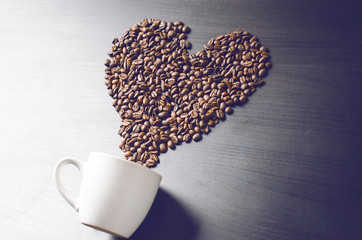 Heart consist from coffee beans. Coffee roasted beans on a shape like a heart and coffee cup. Rustic background. Energy. 