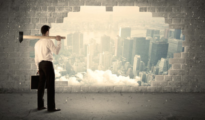 Business man hitting wall with hammer on city view