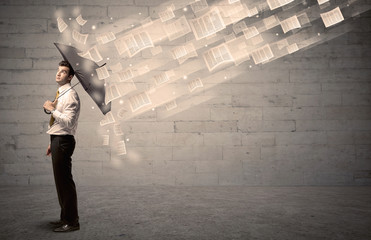 Business man protecting with umbrella against wind of papers