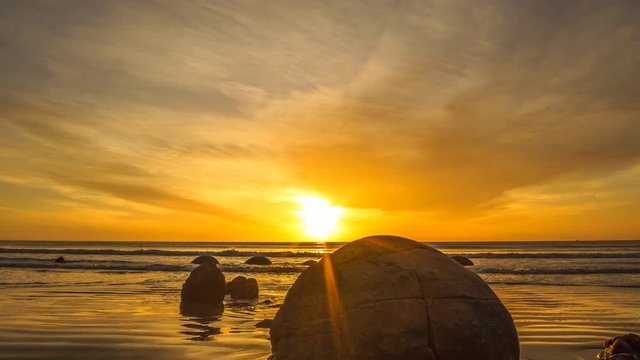 Vibrant Sunrise At Moeraki Boulders- Timelapse. Moeraki Boulders are a group of large spherical stones that have been exposed through shoreline erosion on Koekohe Beach near Moeraki. Zoom In 