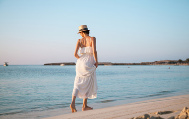 Fototapeta na wymiar Happy woman in a white sundress walking by the beach