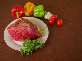 Raw beef joint on a plate and some vegetables.
