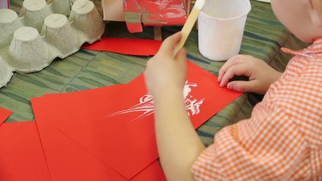 Little boy gluing some red paper at nursery.