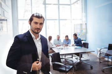 Confident businessman standing against coworkers