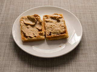 Waffle on a plate with peanut butter spread.