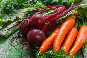 A bunch of young organic carrots and beets with leaves on a wooden table. Vegetables from the garden
