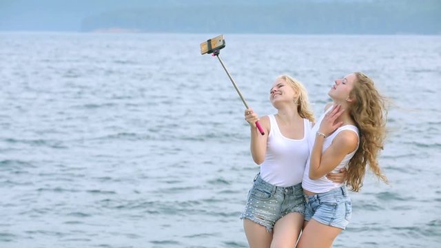 Two friends women taking selfie with mobile phone near the river. Two young girls enjoying near river and taking selfie using smart phone.