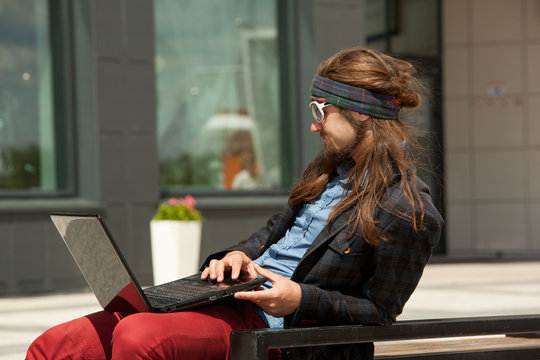 Young hipsters with the computer sits on a bench.