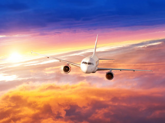 Naklejka na ściany i meble Airplane flying above clouds in dramatic sunset