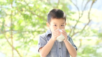 Little boy drinking milk in the park with sunshine in background