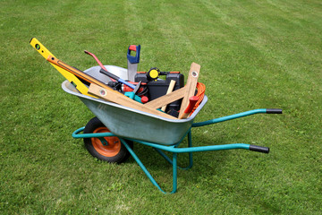 Wheelbarrow with construction tools on green grass