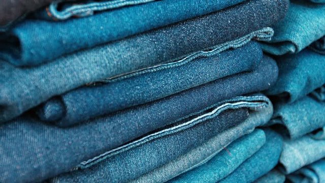 Video 1080p - Many pairs of denim trousers in various shades of faded blue, folded and neatly stacked in a public market.