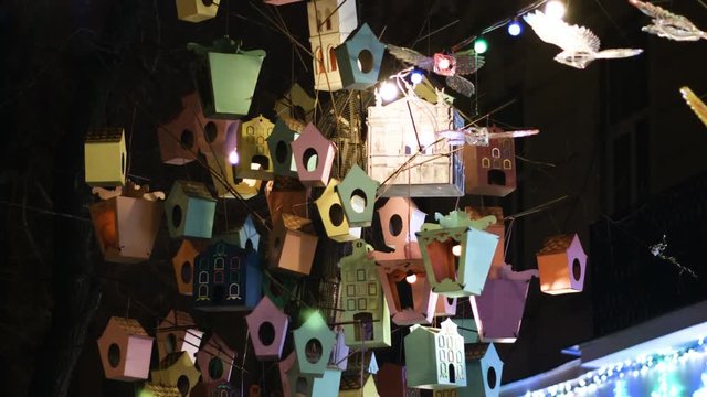A collection of decorative bird houses, wooden feeders on the tree in city
