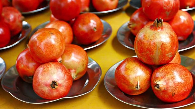 Pomagranate fruit, neatly aranged in sets of four on shiny, metal plates, for sale to customers at a public market.