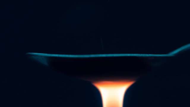 Flame Lighter heats heroin in a spoon on black background. Macro