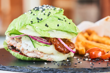 A Burger consisting of lettuce and vegetables, served with French fries on a stone Board