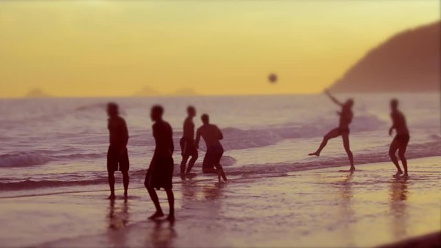 Defocus silhouettes of carioca Brazilians playing altinho futebol beach football kicking soccer balls in the waves on Ipanema Beach in Rio de Janeiro, Brazil