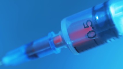 A syringe filling injection blood on a blue background. Macro