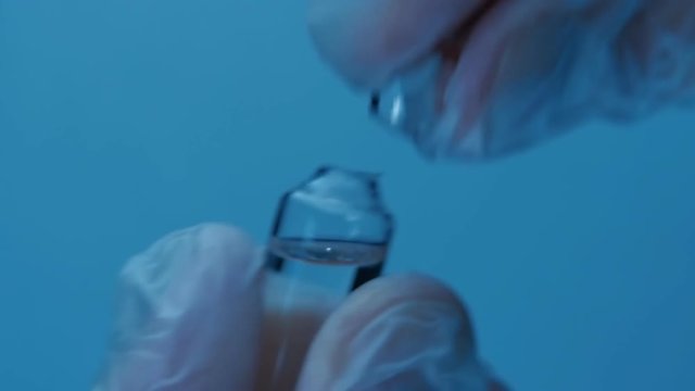 Hand in medical gloves open vial with a medicine on a blue background. Macro