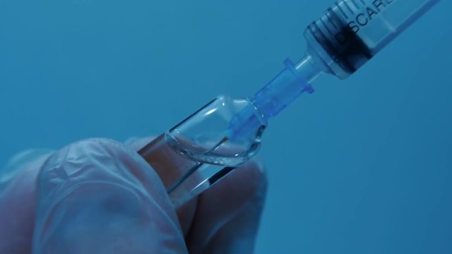 Nurse taking vaccine into a syringe from a glass vial on a blue background.Macro