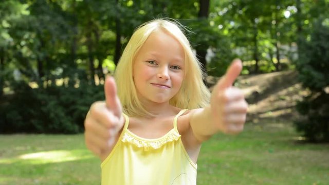 little happy girl shows thumbs up in the park near by the city - support - close up