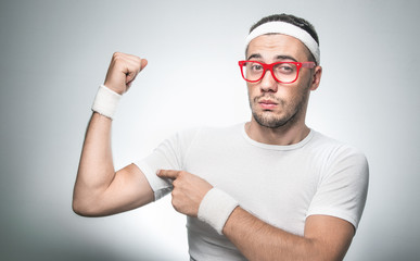 Nerd showing his small biceps, weakly young man, isolated on gray backgorund