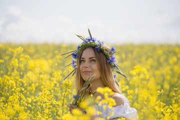 Naklejka na ściany i meble girl with a wreath of colorful flowers on her head, in a flowering yellow field