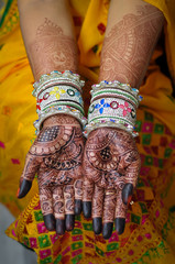 Woman with henna wedding design on both hands with bangle and yellow dress
