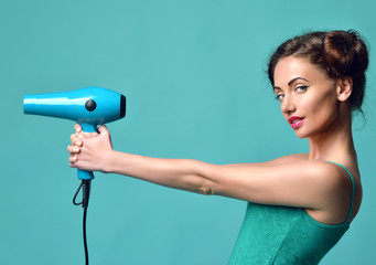Happy young curly brunette woman with hair dryer on blue mint ba