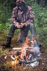 A man warms himself by the fire in the forest, rain, autumn