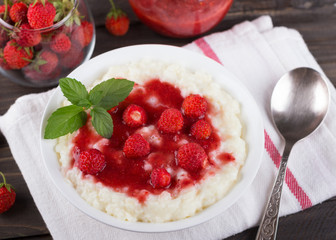 Creamy rice pudding with strawberry jam and fresh strawberries on a wooden table